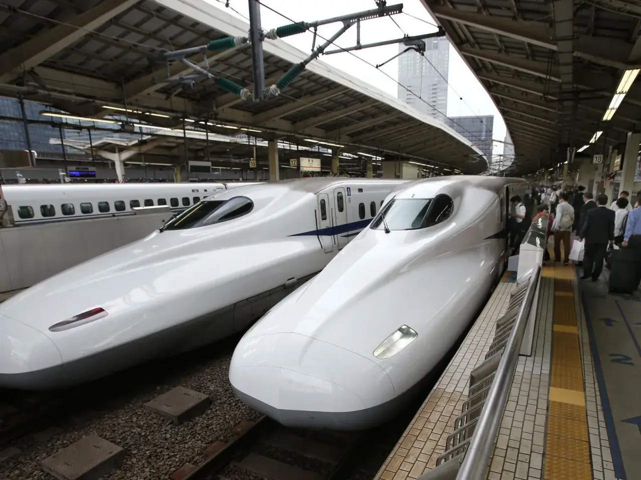 Zwei weiße Shinkansen-Züge stehen nebeneinander auf einem Bahnhof. Sie sind ein Symbol für die effizienten Zugverbindungen Japans.