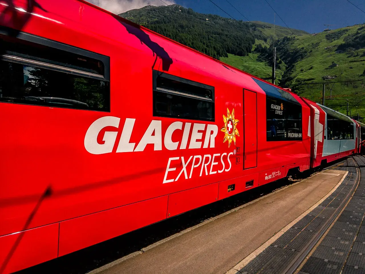 Der rote Glacier Express fährt durch eine grüne Berglandschaft.