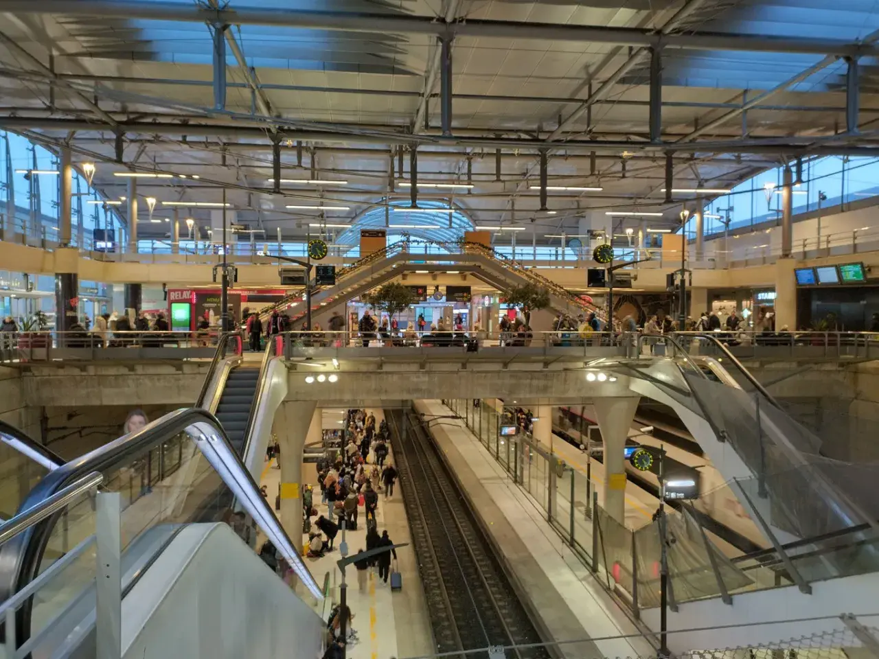 Menschenmassen auf einem Bahnhof, bereit für die Reise mit dem Zug nach Disneyland Paris. Rolltreppen und Bahnsteige sind voller Reisender.