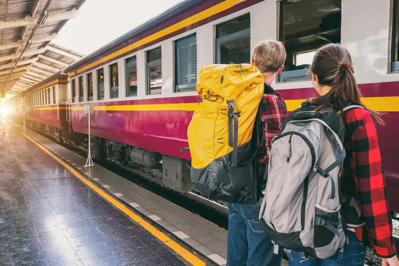 Zwei Rucksacktouristen warten am Bahnsteig auf ihren Zug. Die Reise beginnt, ein internationales Abenteuer.