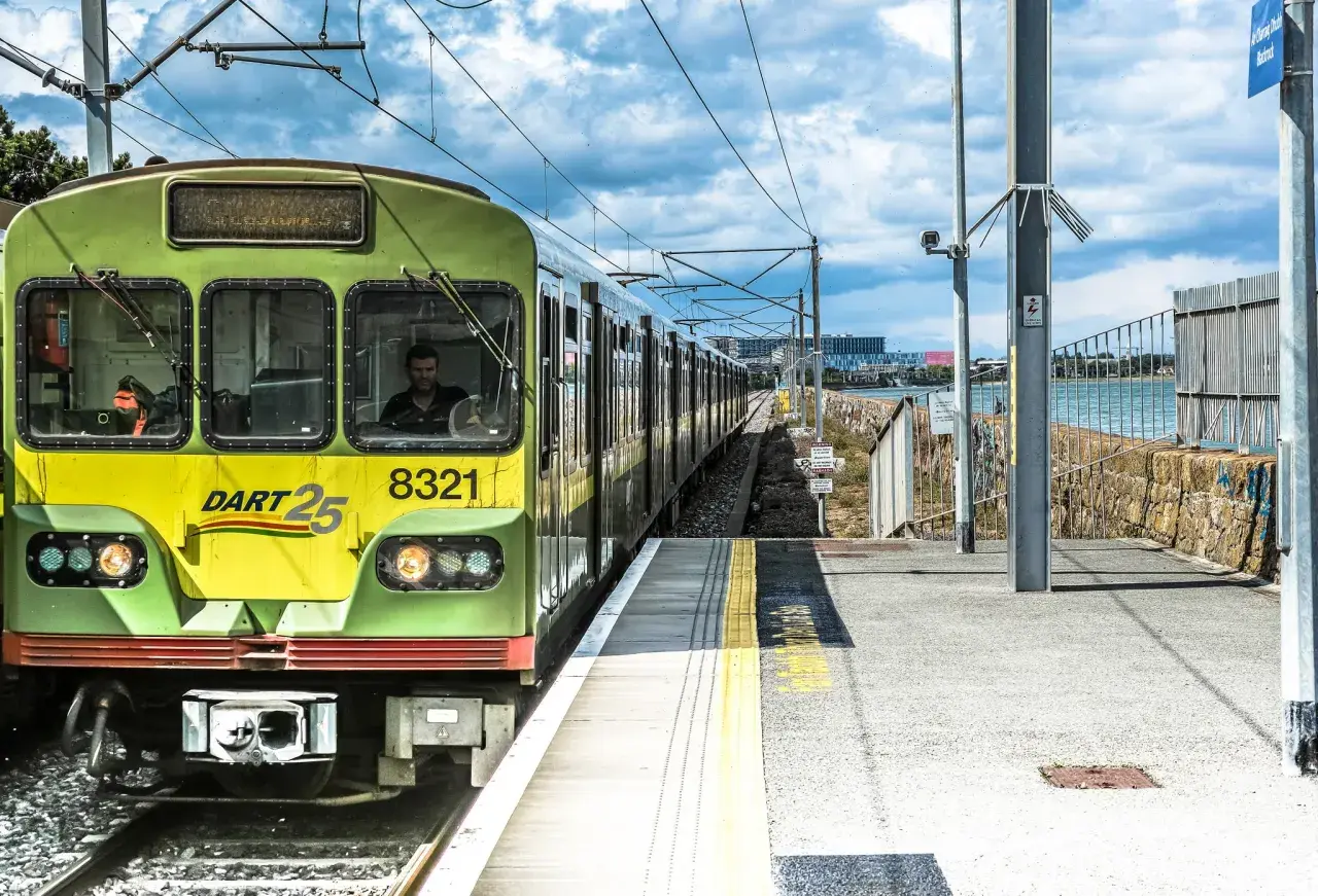 Grüner irischer Zug DART 25 mit der Nummer 8321 fährt auf einer Strecke am Meer entlang.