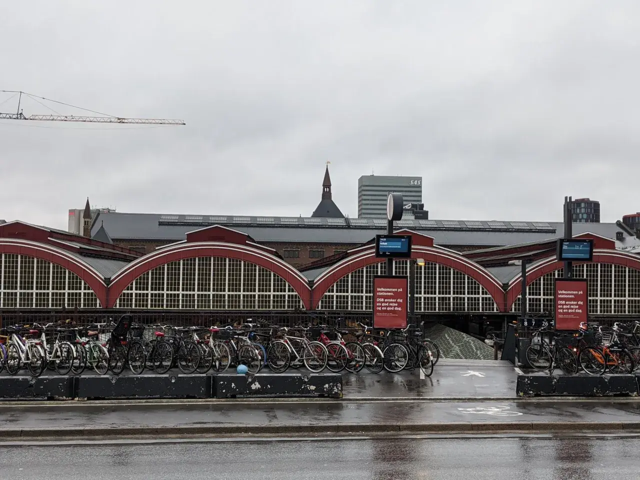 Fahrräder vor dem historischen Hauptbahnhof Kopenhagen. Ein Kran ragt in den grauen Himmel.