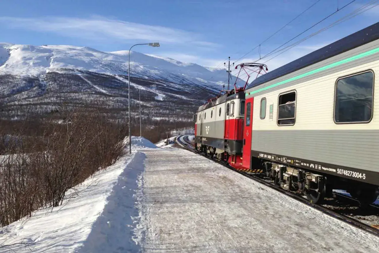 Der Zug von Stockholm nach Kiruna fährt durch eine verschneite Winterlandschaft mit schneebedeckten Bergen im Hintergrund.