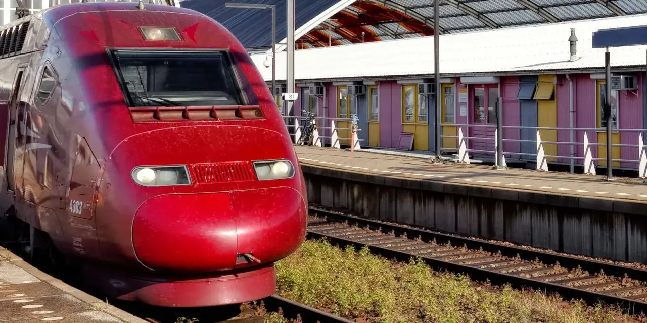 Roter Zug am Bahnsteig, bereit für die Fahrt von Hannover nach Paris. Bunte Gebäude im Hintergrund.