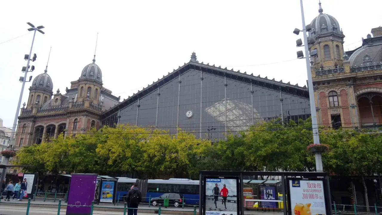 Budapest train station mit seiner beeindruckenden Glasfassade und den historischen T&uuml;rmen. B&auml;ume s&auml;umen den Platz vor dem Bahnhof.