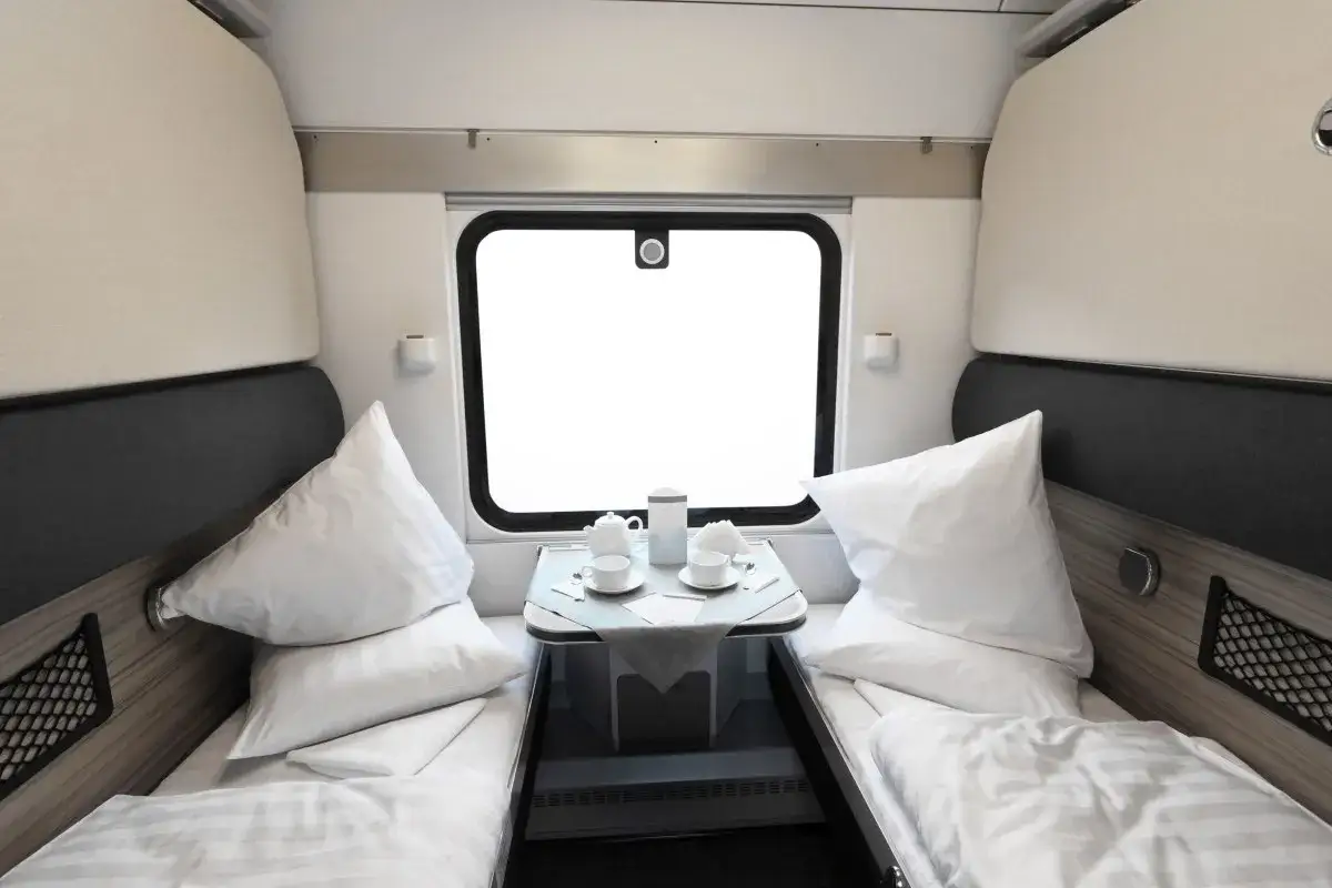 Gem&uuml;tliche Schlafkabine f&uuml;r die Reise von Hamburg nach Z&uuml;rich. Zwei Betten mit wei&szlig;en Kissen und Decken, ein Tisch mit Tee-Service vor dem Fenster.