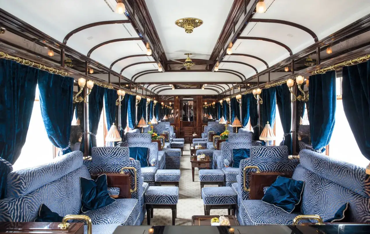 Luxuriöser Salonwagen des Orient Express mit blauen Samtvorhängen und blau-weiß gemusterten Sitzmöbeln.