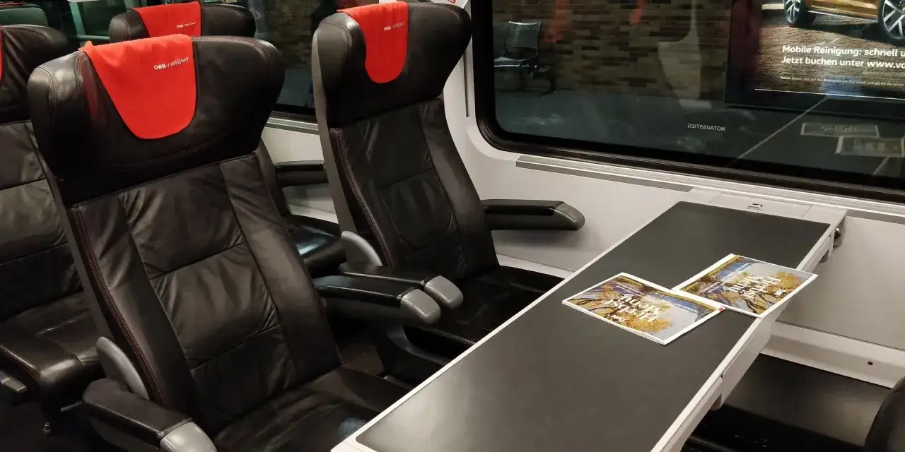 Bequeme Ledersitze im rj bahn Zug mit roten Kopfst&uuml;tzen. Auf dem Tisch liegen Brosch&uuml;ren.