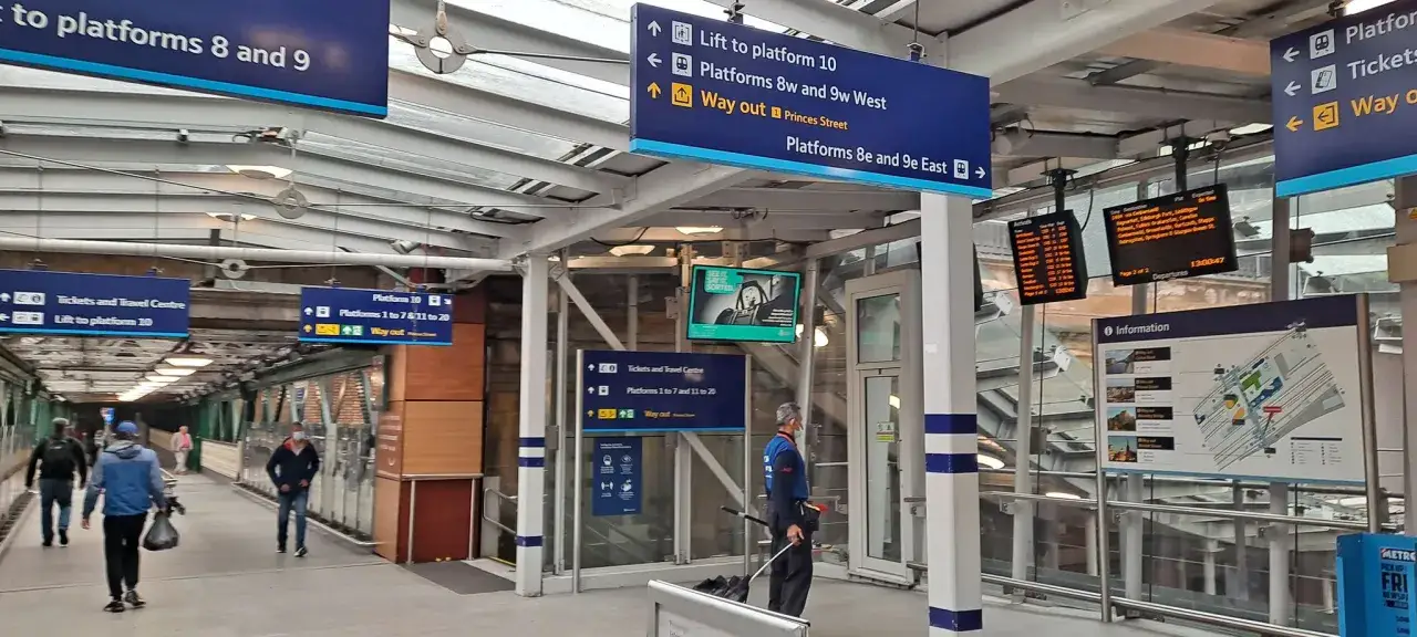 Bahnhofsschilder weisen den Weg zum Zug nach Edinburgh. Reisende eilen über den Bahnsteig.