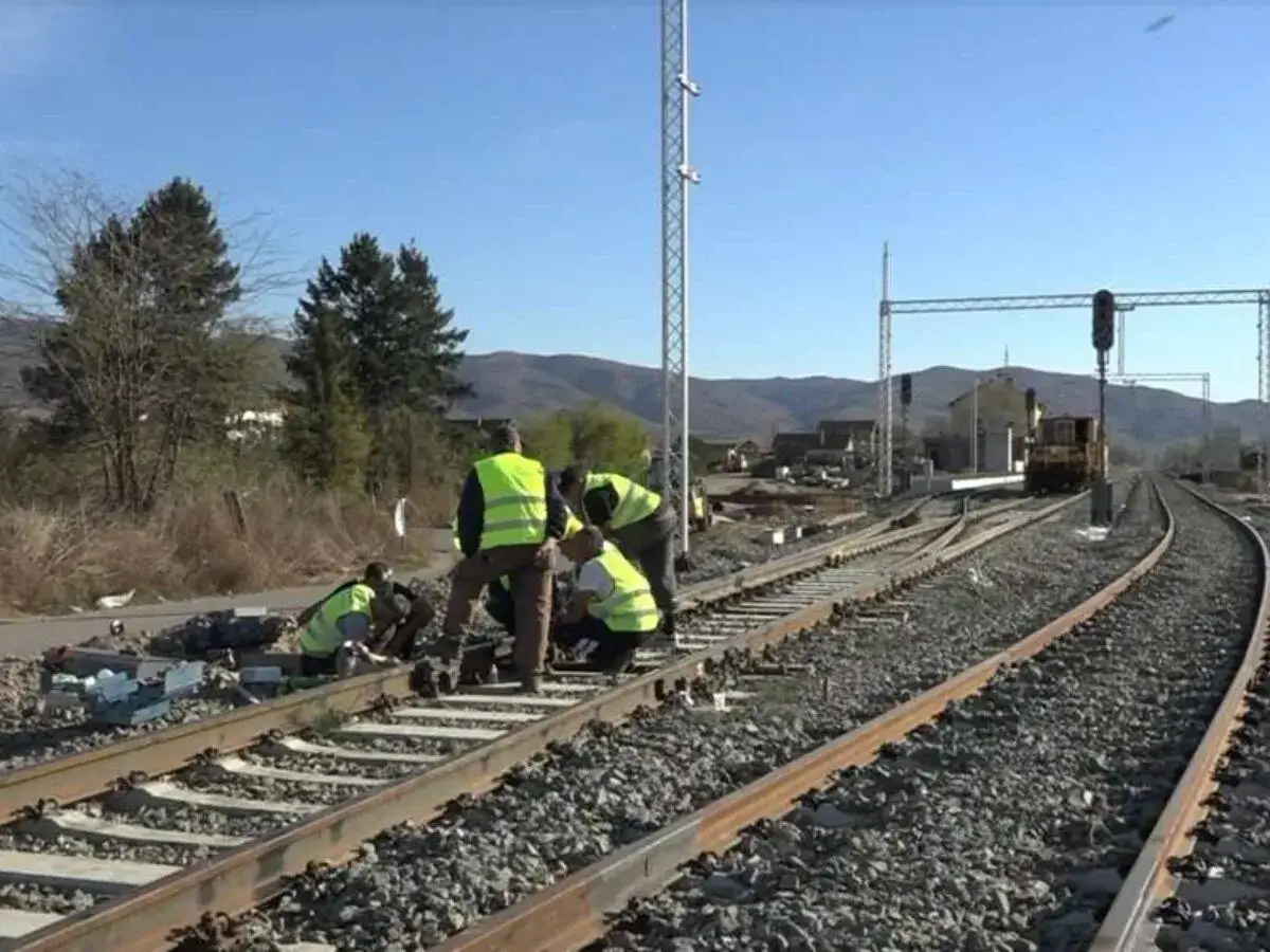 Arbeiter in Warnwesten reparieren Gleise der serbischen Eisenbahnen. Ein gelber Zug steht im Hintergrund.