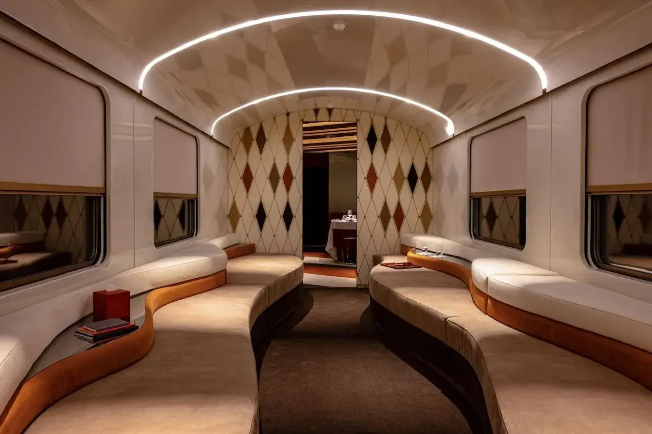 Luxuriöses Interieur eines Waggons, inspiriert vom Orion Express. Geschwungene Sofas und ein Rautenmuster an der Wand schaffen eine elegante Atmosphäre.