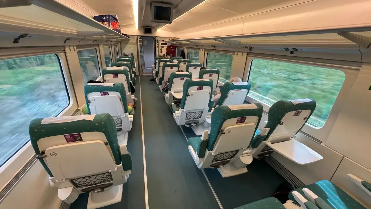 Innenraum eines Renfe Alvia Zuges mit grünen Sitzen und ausklappbaren Tischen.