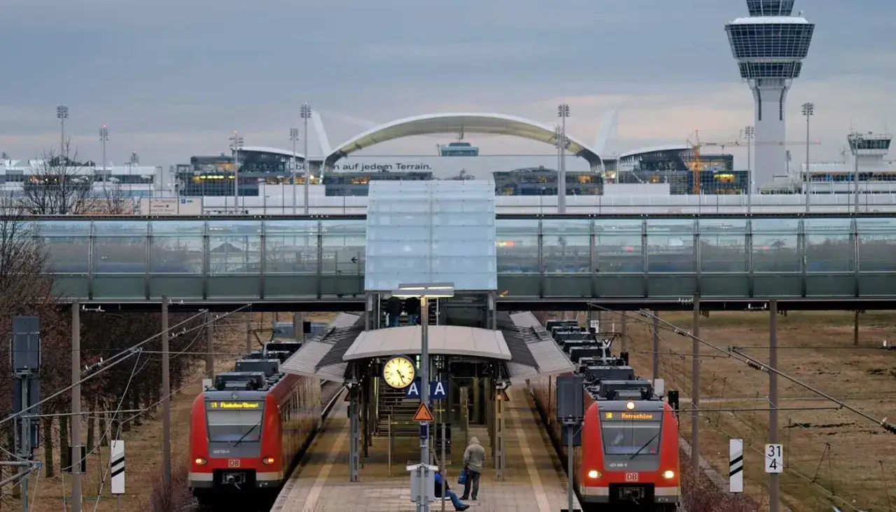 Zwei rote S-Bahnen warten am Bahnsteig. Im Hintergrund der moderne Flughafen München mit seinem markanten Tower.