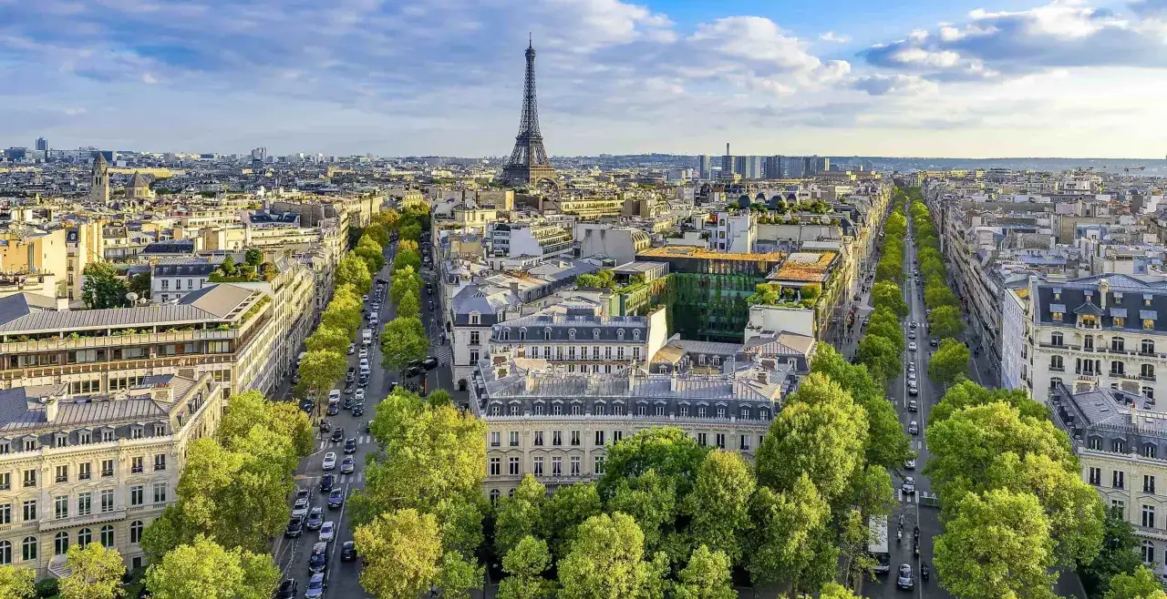 Blick auf Paris mit dem Eiffelturm. Eine Allee mit Bäumen und Autos führt zum Wahrzeichen. Der TGV von Luxemburg nach Paris ist eine schnelle Verbindung.