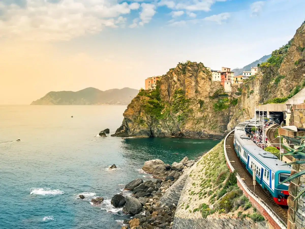Mit dem Zug ans Meer Italien: Ein Zug f&auml;hrt entlang der felsigen K&uuml;ste Italiens, vorbei an bunten H&auml;usern und dem t&uuml;rkisfarbenen Meer.