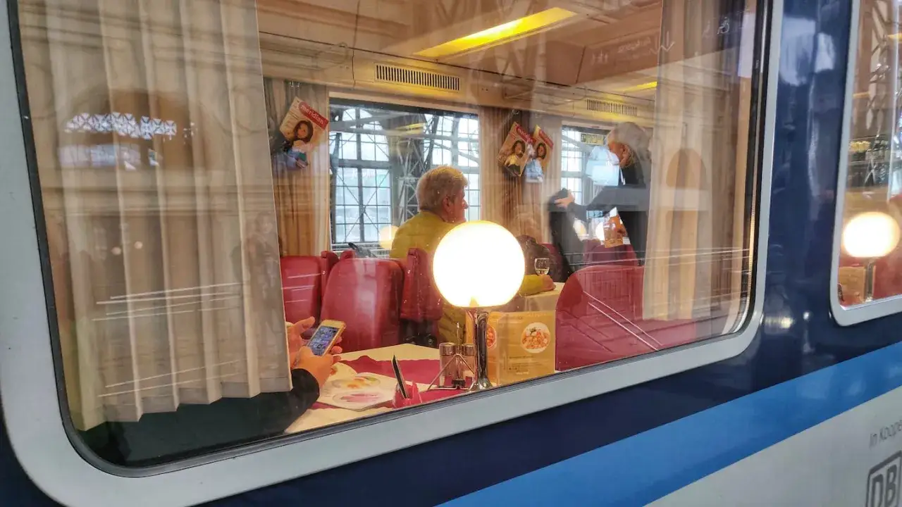 Gemütliche Zugfahrt von Berlin nach Prag. Eine Frau blickt aus dem Fenster, während ein Mann am Tisch sitzt.