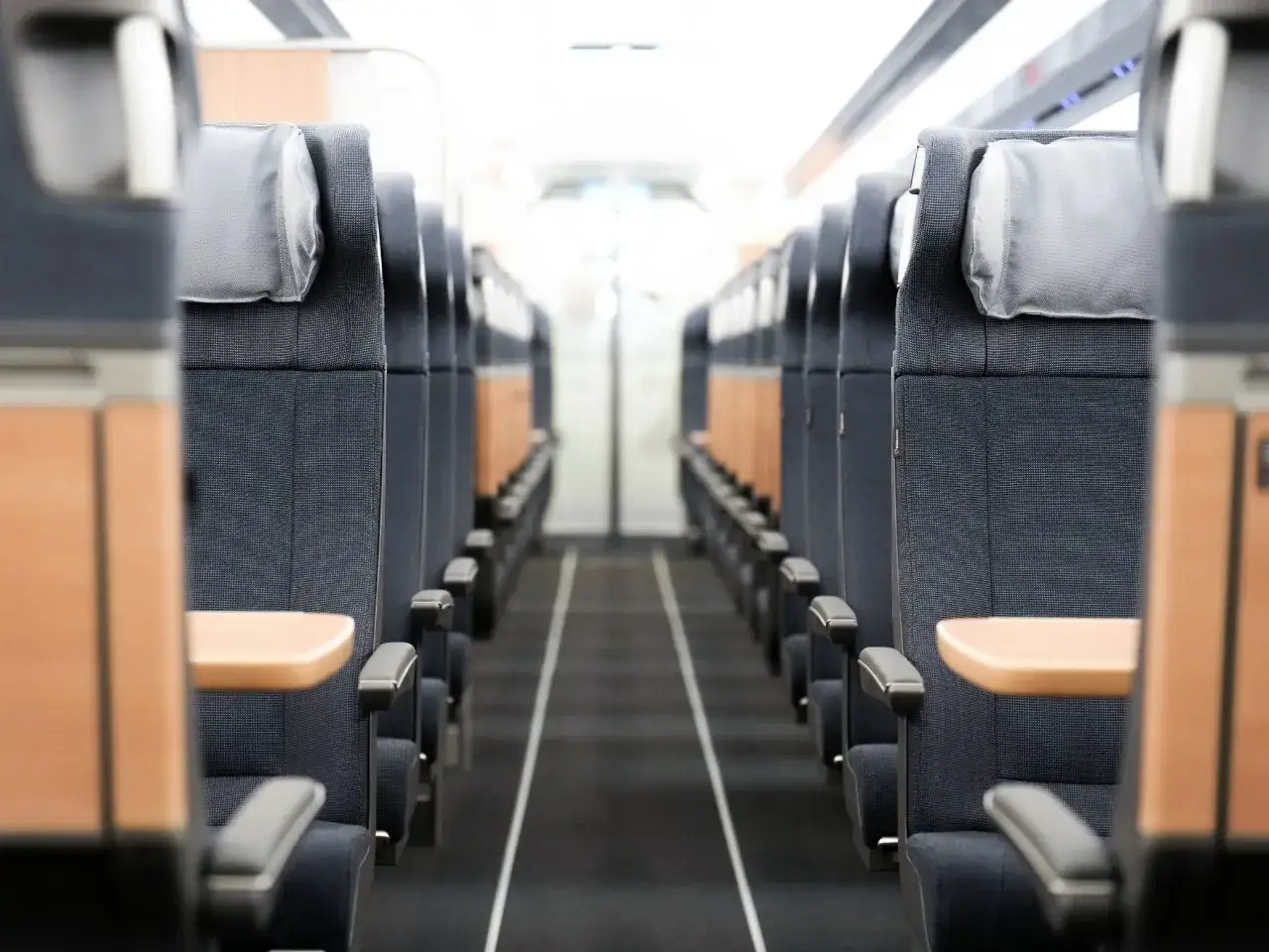 Reihe von Sitzen in einem Zug. Die Sitze sind dunkelblau mit hellgrauen Kopfst&uuml;tzen und Holzakzenten. Der Gang ist mit einem schwarzen Teppich ausgelegt. Der Zug ist bereit f&uuml;r den ice service.