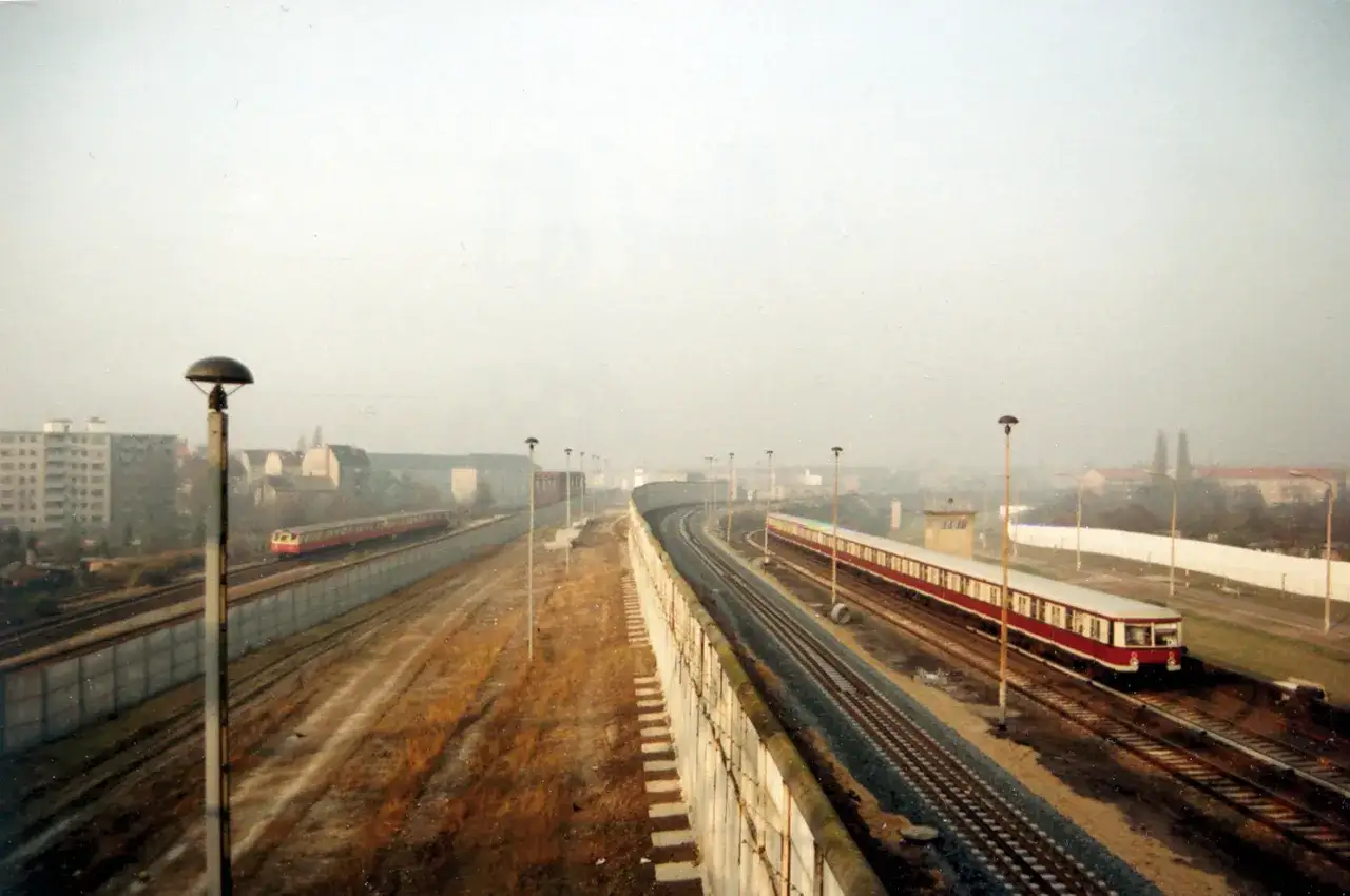 Zwei Bahnen fahren parallel, eine davon auf der anderen Seite der Mauer. Ein Symbol f&uuml;r den nahenden bahn mauerfall.