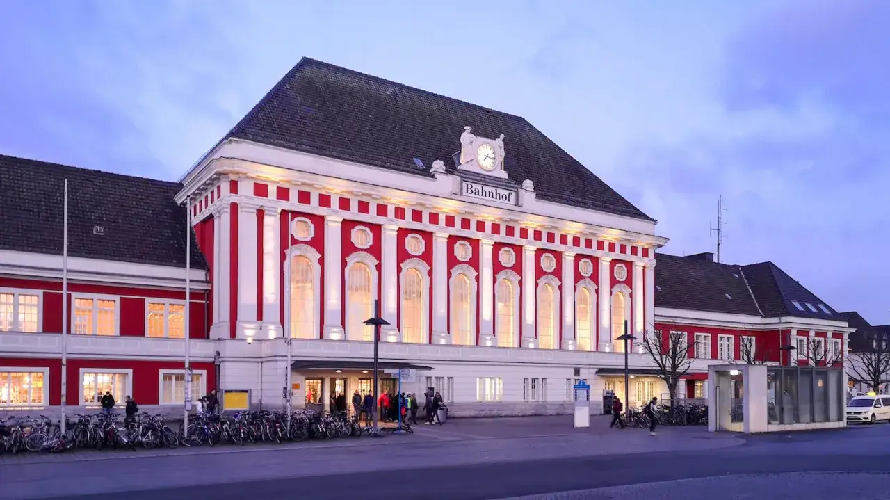 Prachtvoller Bahnhof in Rot und Weiß, beleuchtet im Abendlicht. Viele Fahrräder stehen davor. Ein Kandidat für den besten Bahnhof Deutschlands.