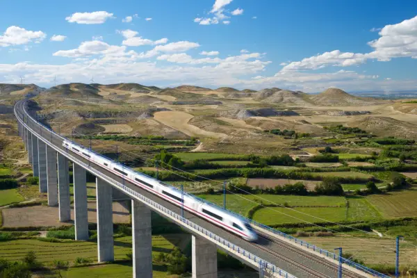 Schneller Zug auf einer Brücke in Spanien, der durch eine hügelige Landschaft mit Windrädern fährt.
