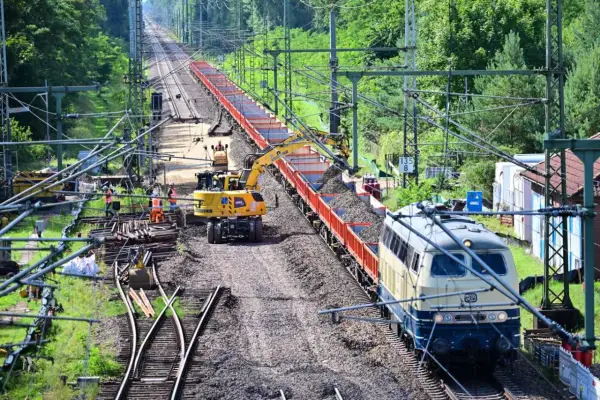 Gleisbauarbeiten: Bagger beladen einen Güterzug mit Schotter.