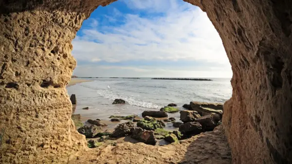 Blick aus einer Höhle am Strand von Rom. Wellen brechen an Felsen.